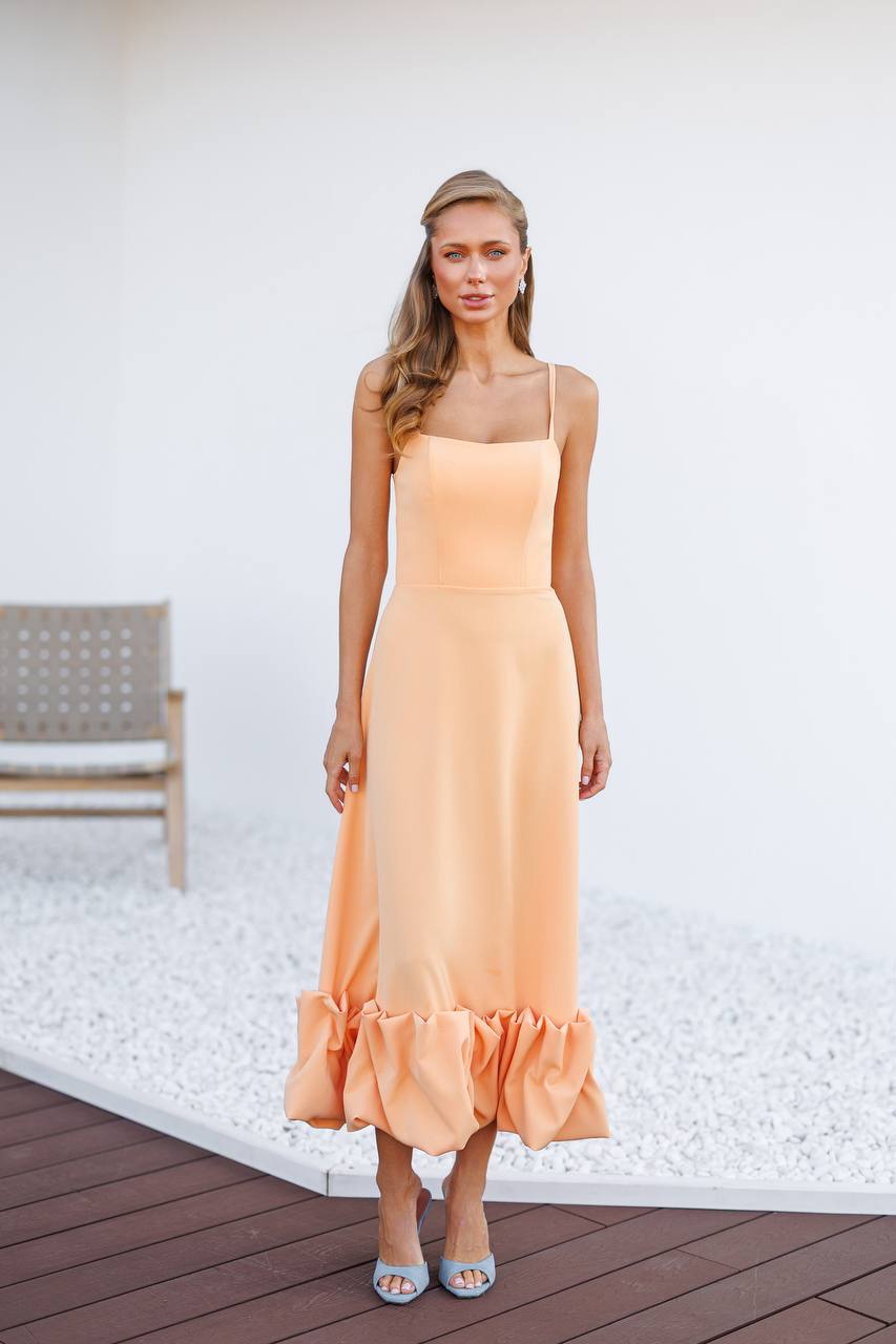Woman wearing a peach dress standing on a wooden deck with a white wall background