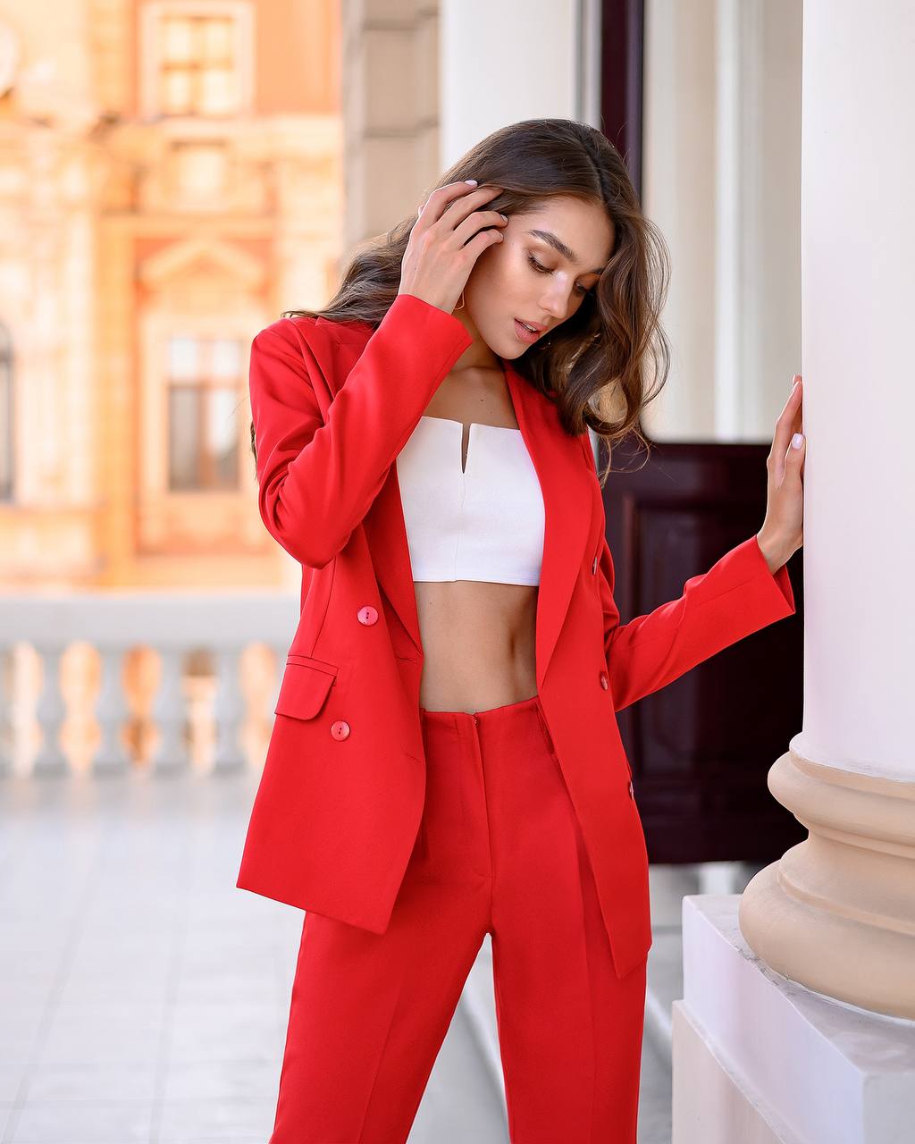 Woman in a red suit standing outdoors with classical architecture in the background