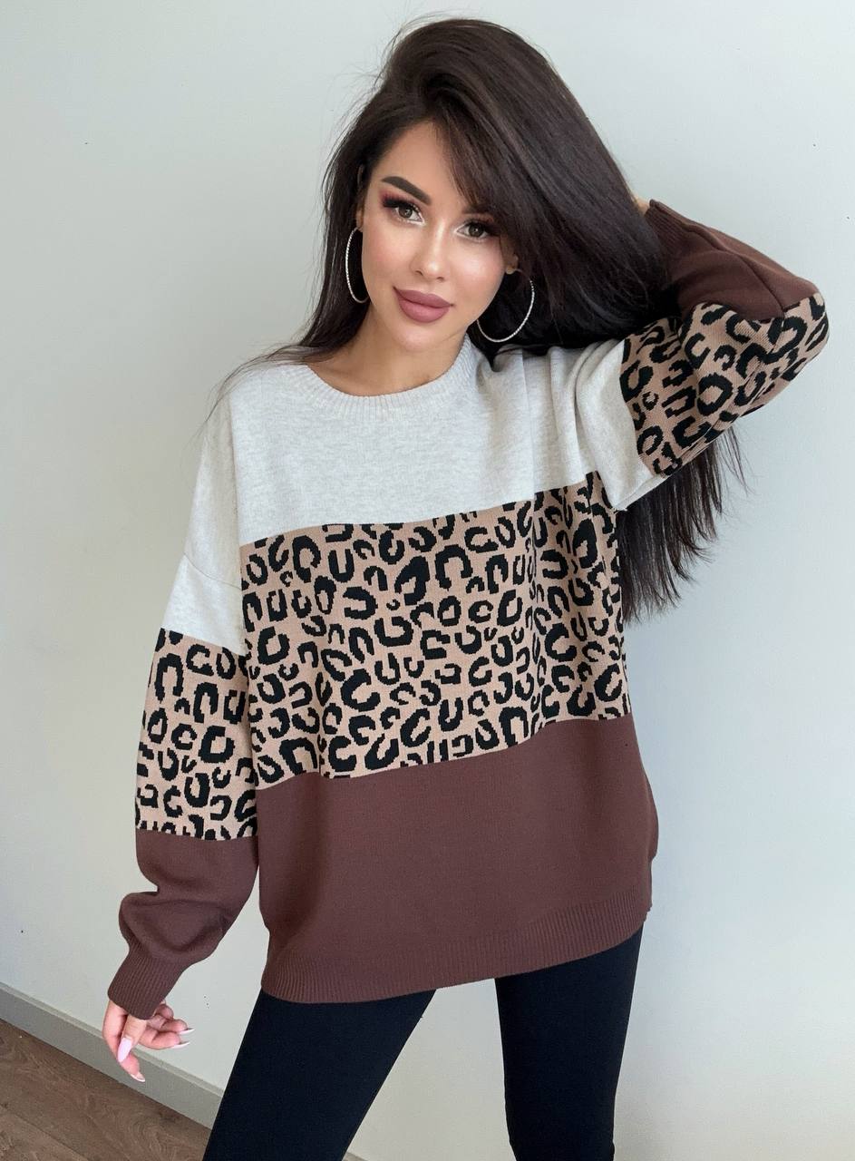 Woman wearing a sweater with leopard print sleeves against a plain background