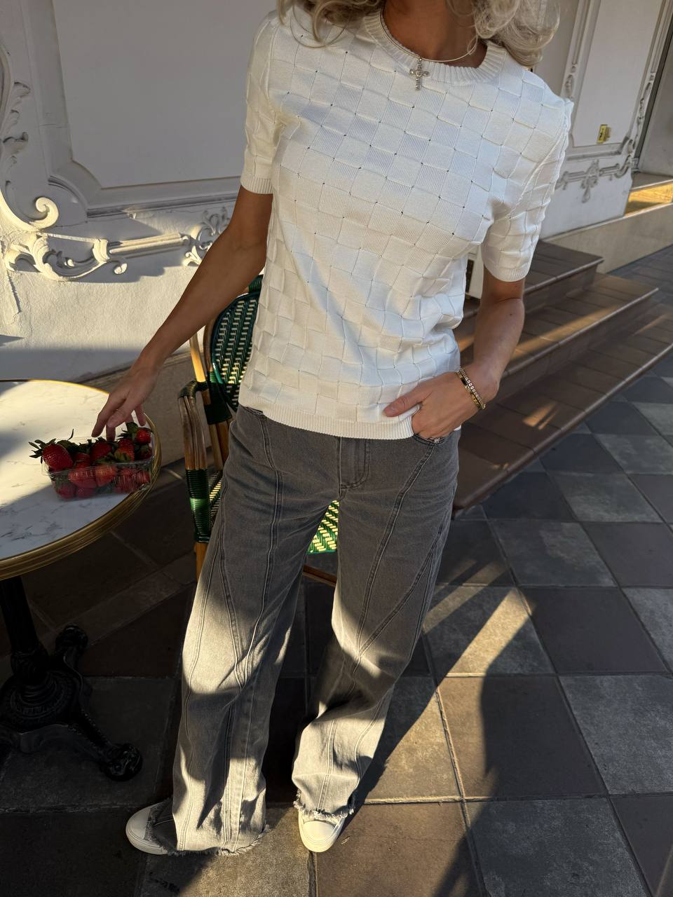 Person wearing a textured white top and gray pants standing on a patio.
