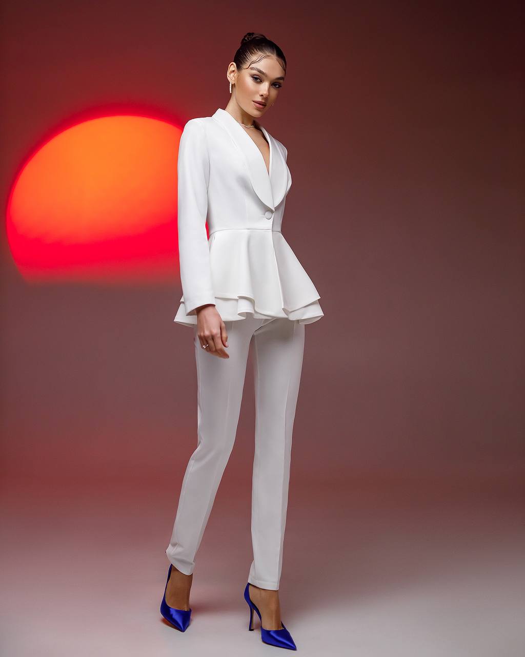 Woman in a white suit with blue shoes against a red and orange sunset background