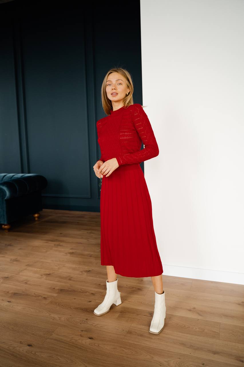 Woman wearing a red dress standing in a room with wooden flooring and a dark blue wall.