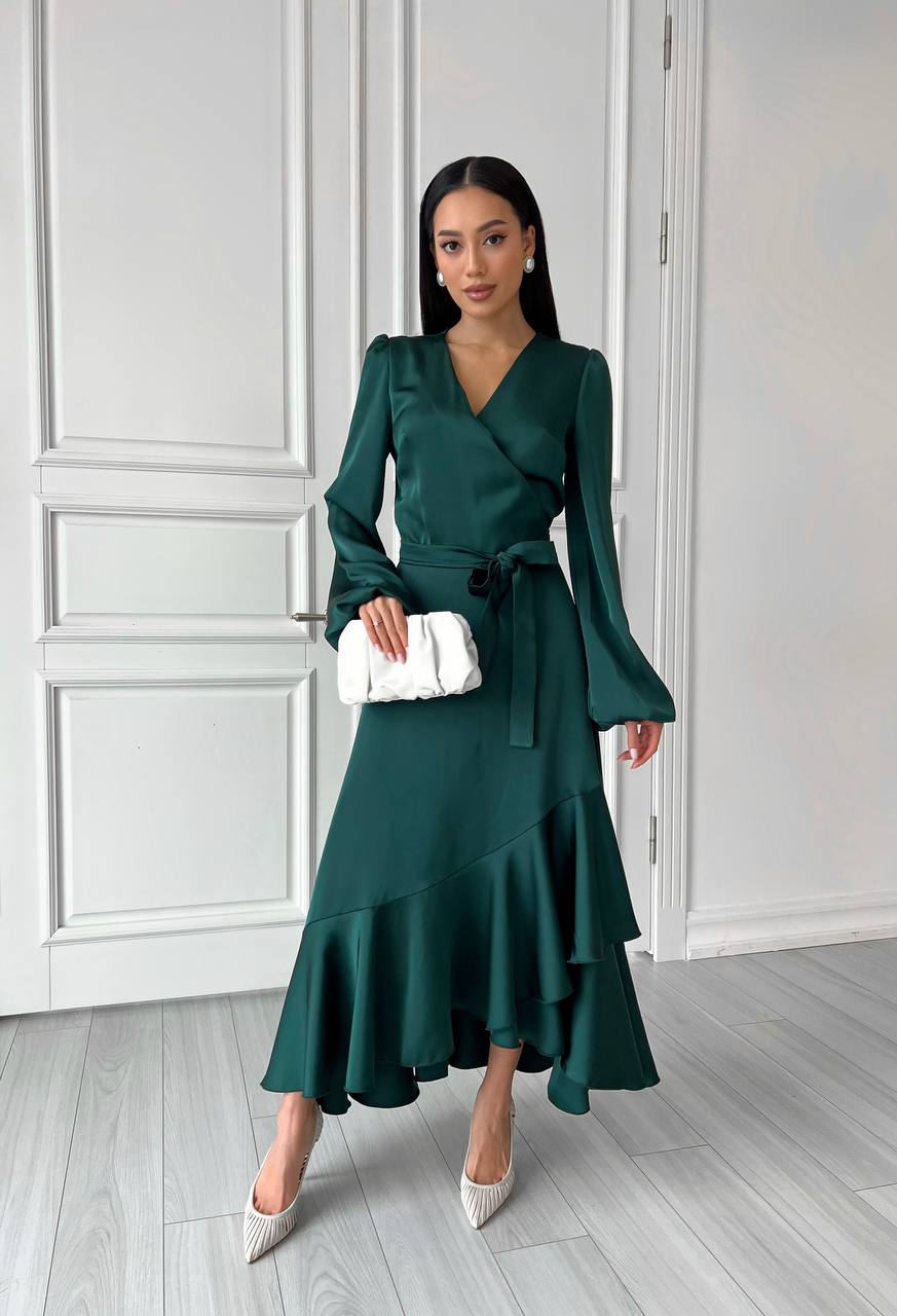Woman in a green dress standing against a white paneled wall.