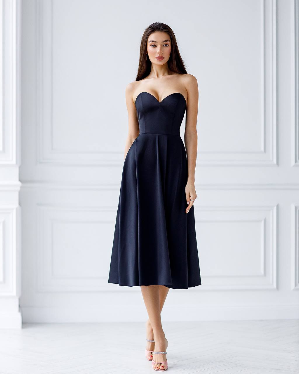 Woman wearing a strapless black dress against a white wall