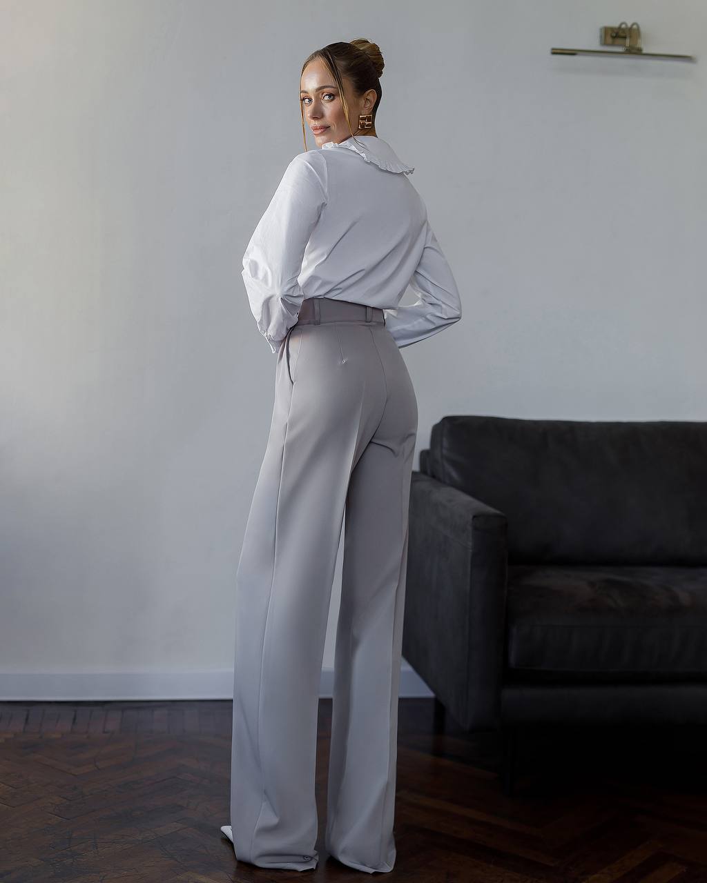 Person wearing a white shirt and gray pants in a room with a dark sofa.