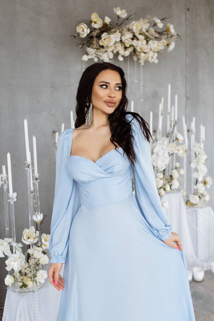 Woman in a light blue dress standing in front of decorative flowers and candles.