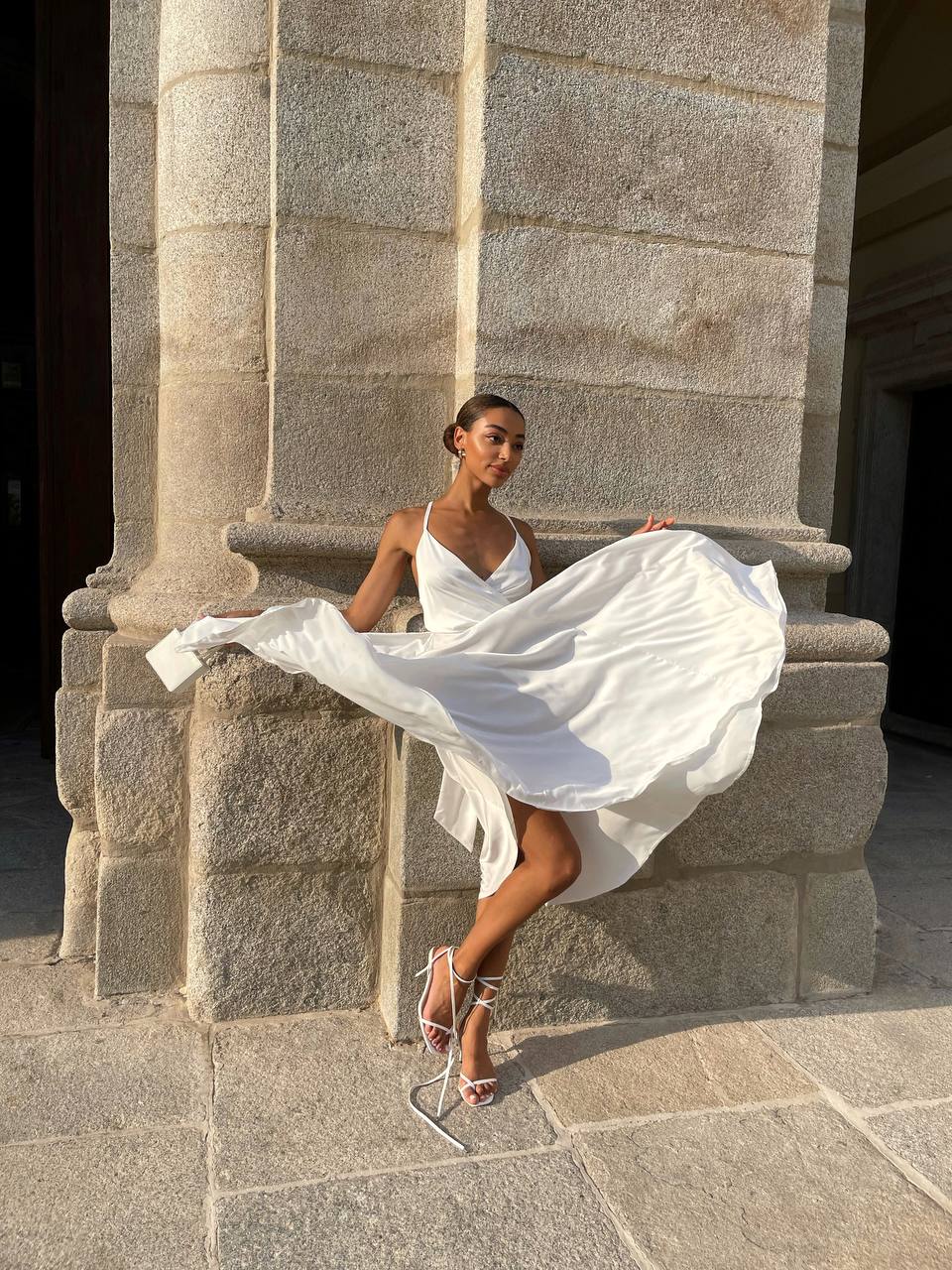 Woman in a white dress sitting against a stone wall
