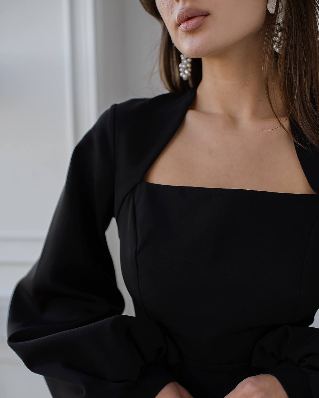 Close-up of a person wearing a black dress with a plain background