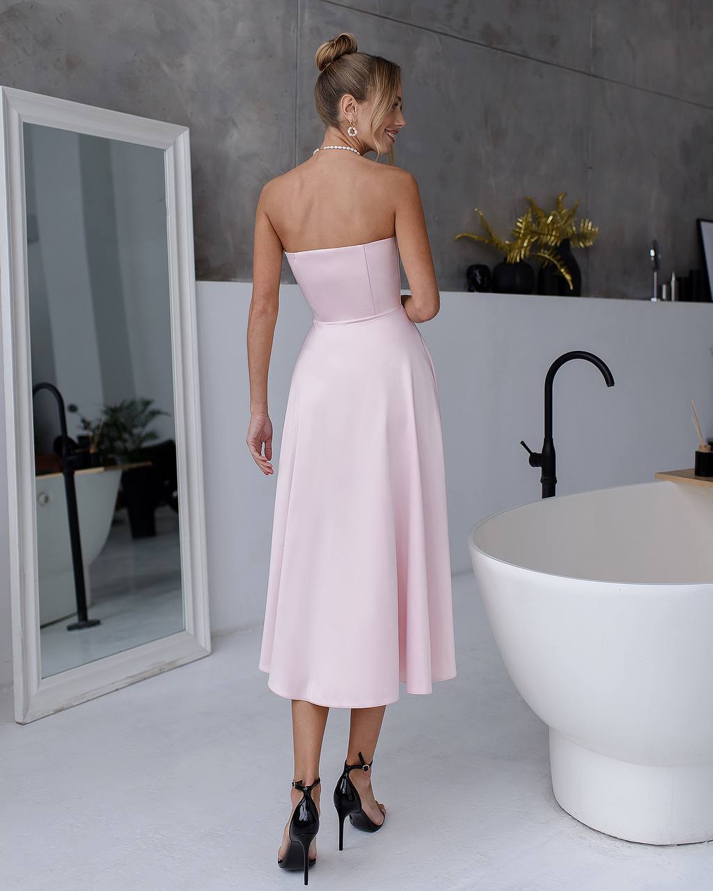 Woman in a light pink strapless dress standing in a bathroom.