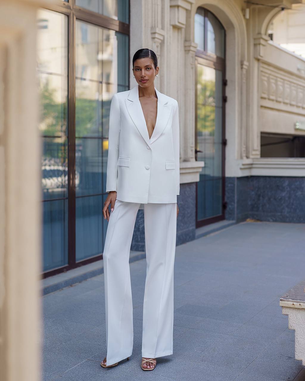 Woman in a white suit standing in front of a building with large windows.