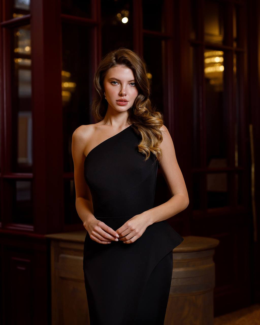 Woman wearing a black one-shoulder dress in a dimly lit room.