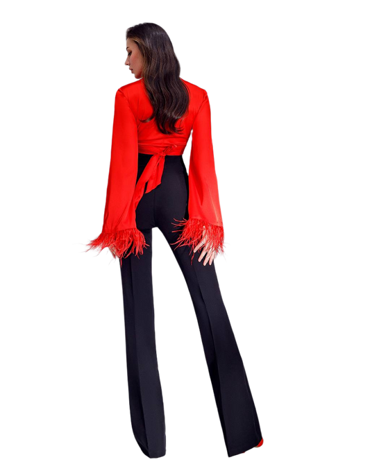 Woman wearing a red blouse with fringe details and black pants on a white background