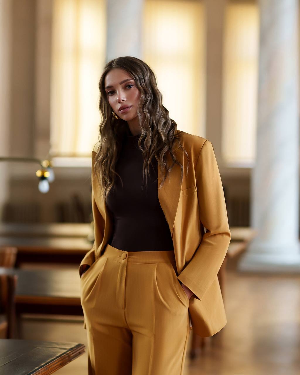 Woman in a mustard yellow suit standing in an indoor setting with blurred background