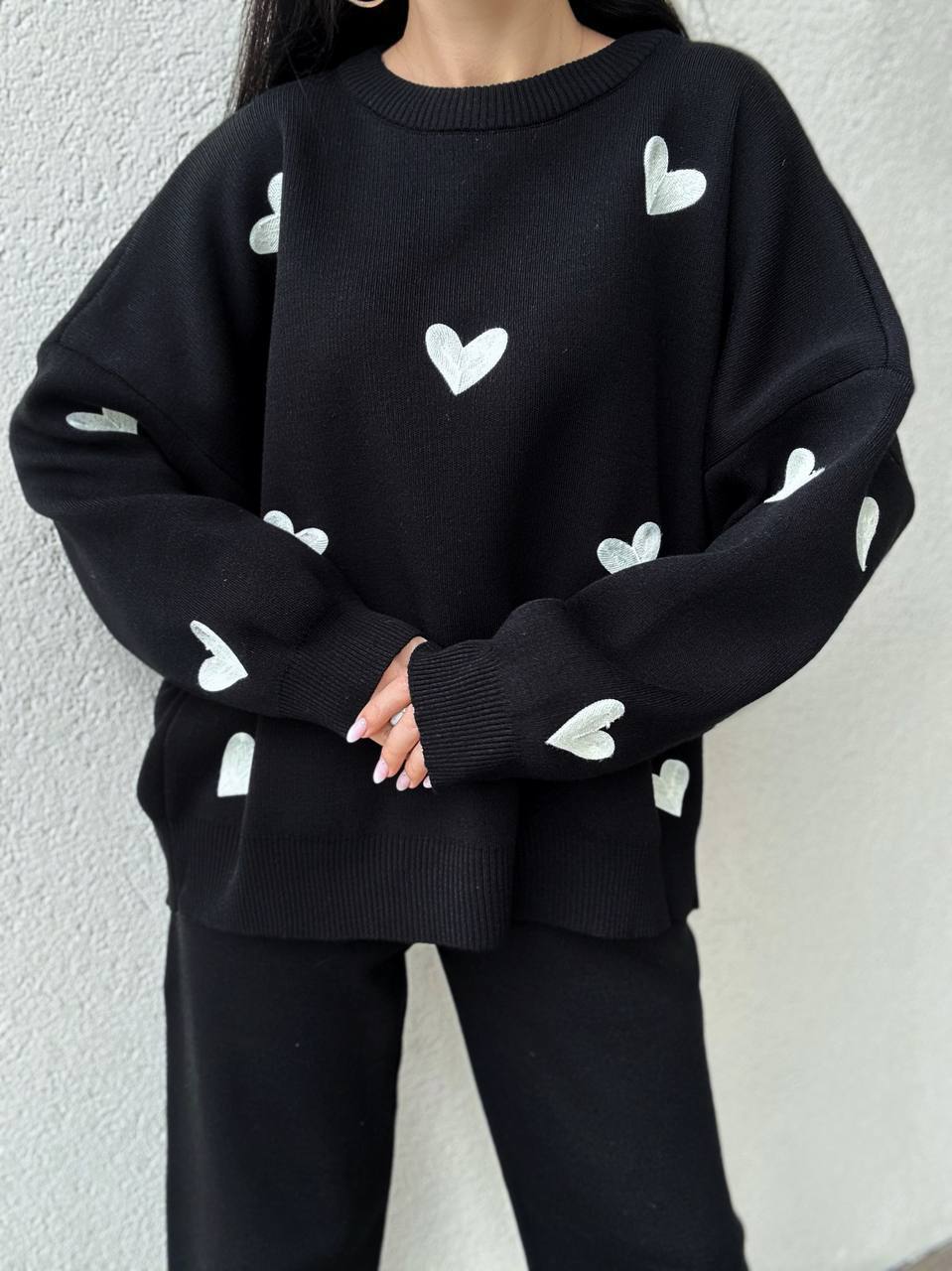 Black sweater with white heart patterns worn by a person against a plain background