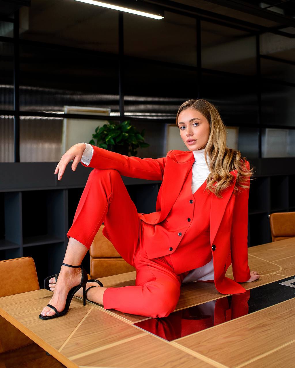 Woman in a red suit sitting on a desk in an office setting