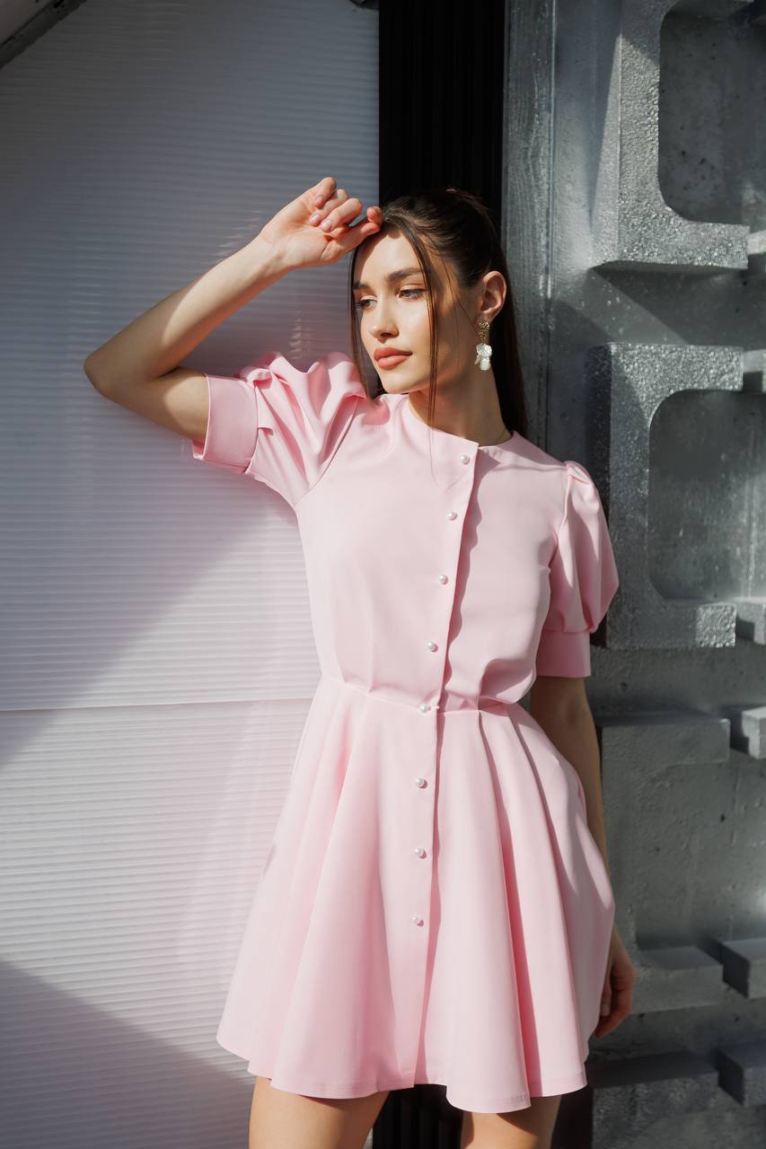 Woman wearing a pink dress standing against a textured wall.
