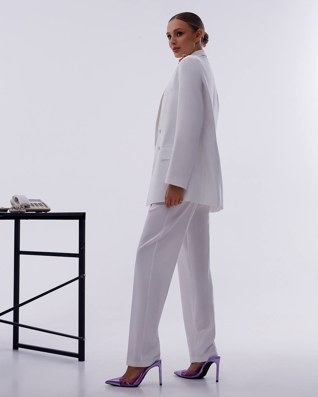 Woman in a white suit standing in a minimalistic office setting.
