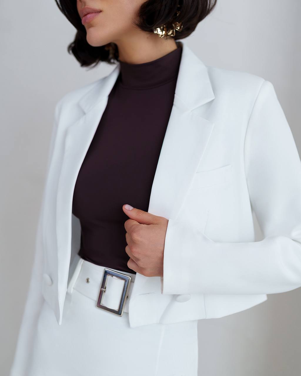 Person wearing a white blazer over a dark top with a plain background