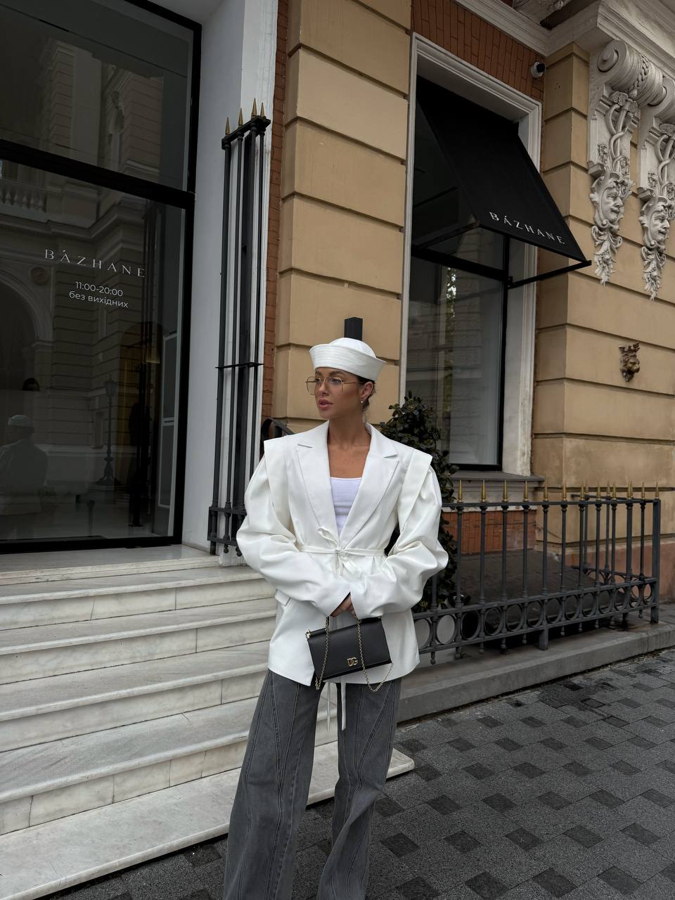 Person wearing a white outfit with a headscarf standing in front of a building entrance.