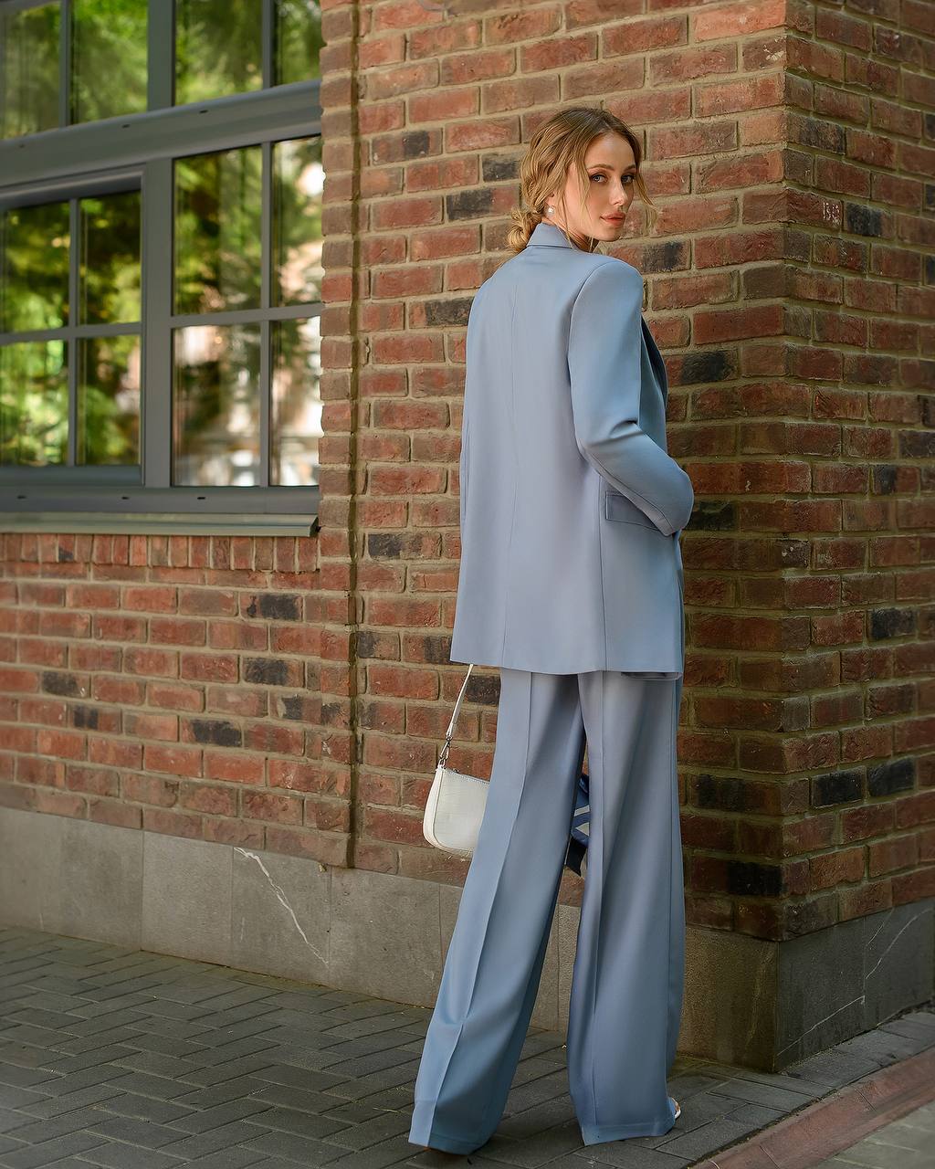 Woman in a light blue suit standing against a brick wall.