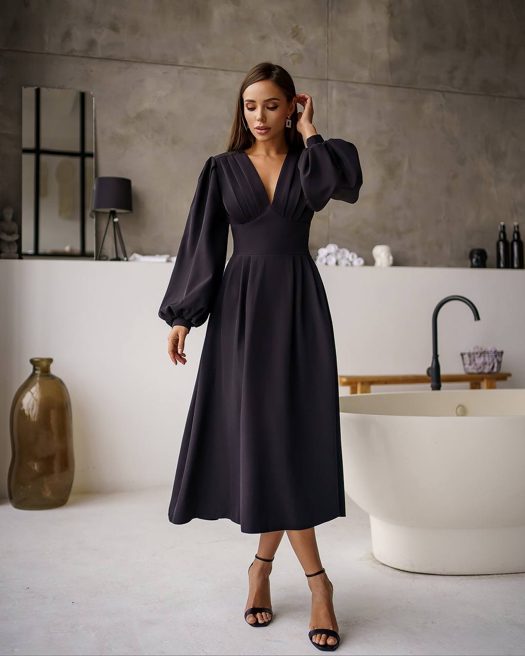 Woman in a black dress standing in a modern bathroom.