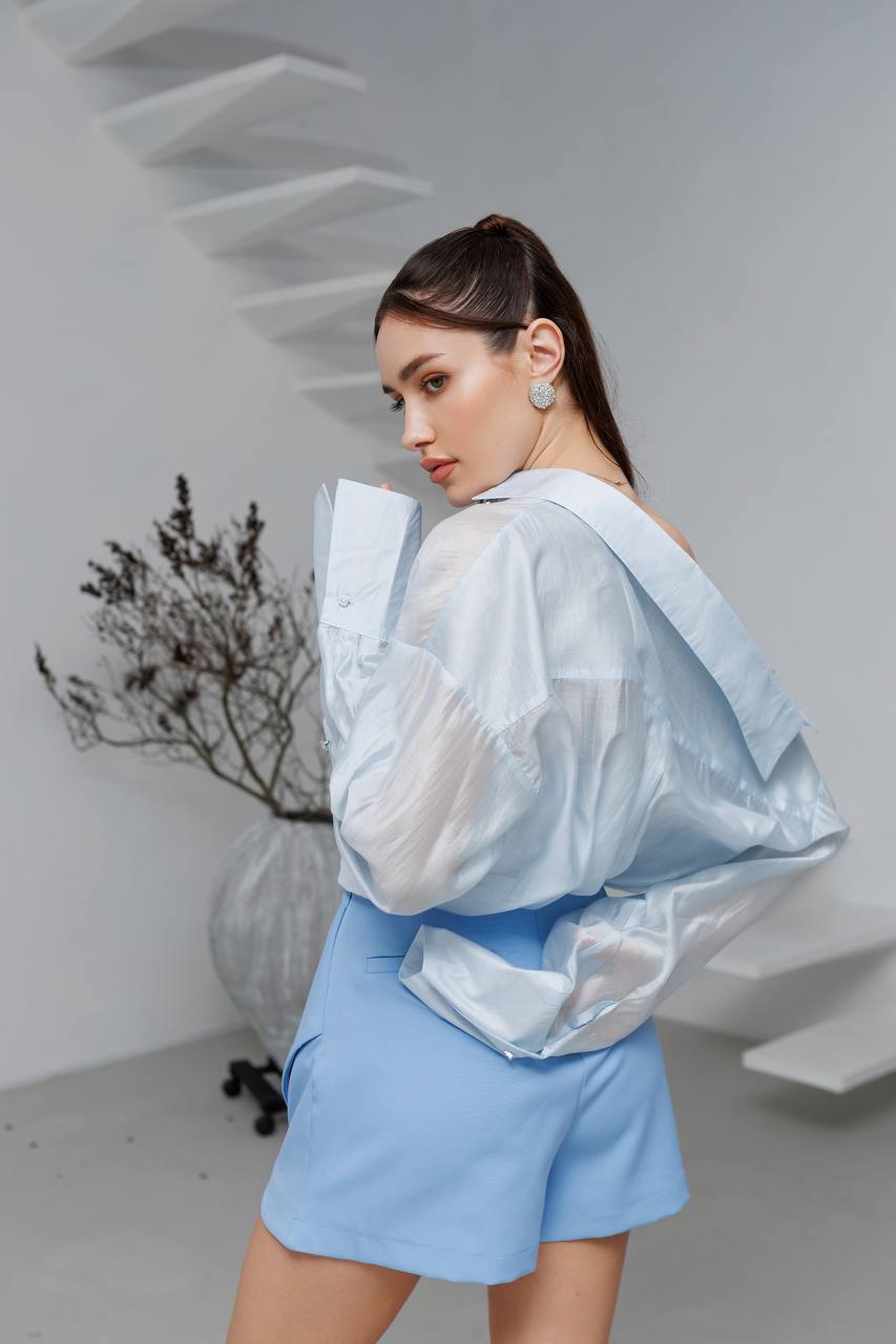 Woman wearing a light blue outfit with a sheer overlay in a minimalistic setting.