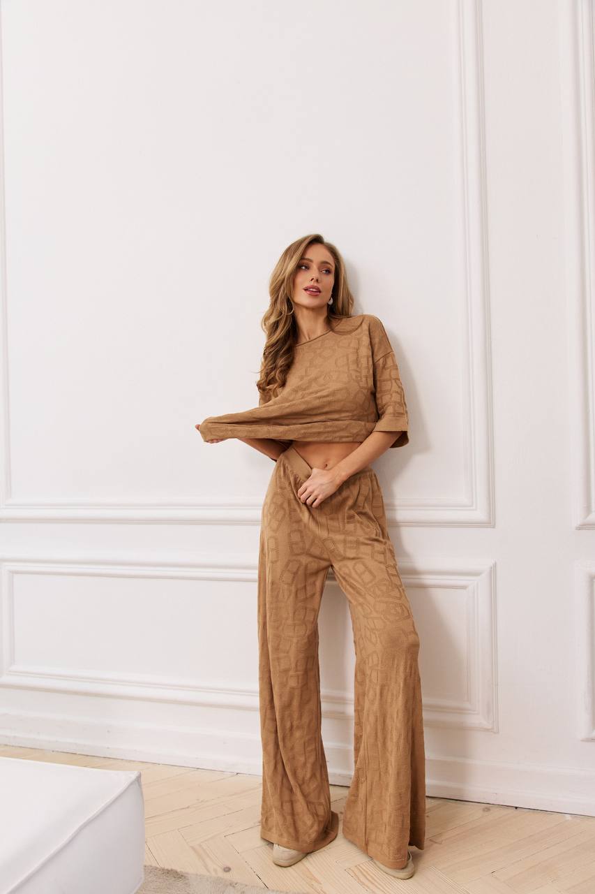 Woman wearing a brown outfit against a white paneled wall.