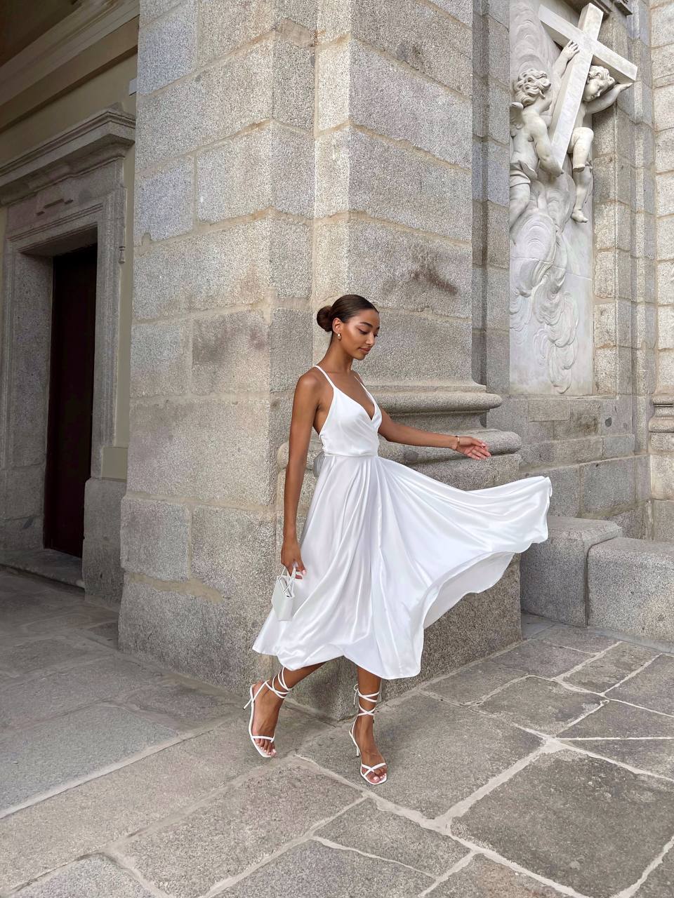 Woman in a white dress walking in front of a stone building with sculptures.