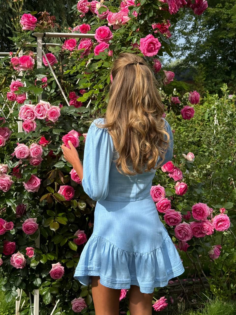 Woman in a blue dress standing among pink roses in a garden