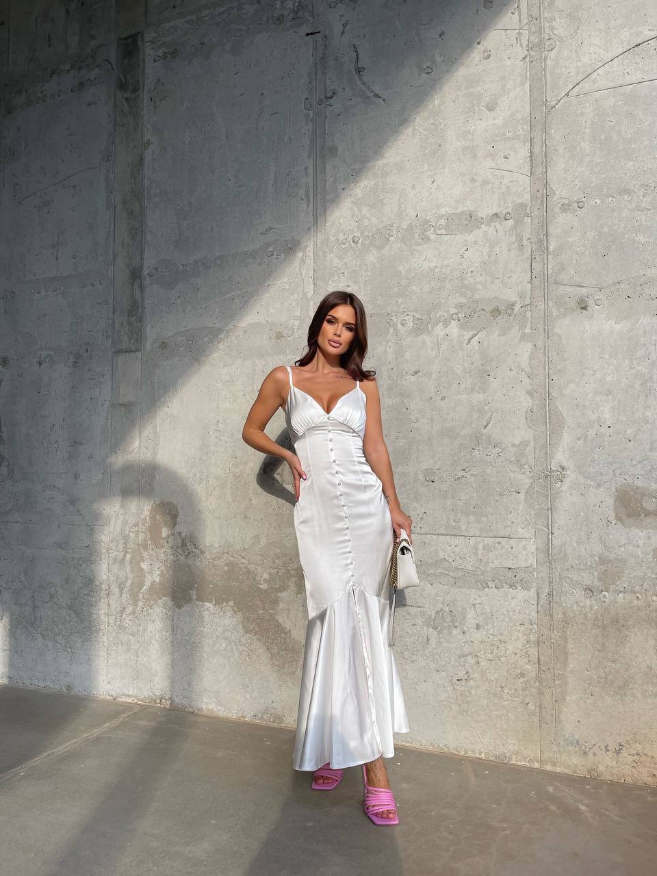 Woman in a white dress standing against a concrete wall.