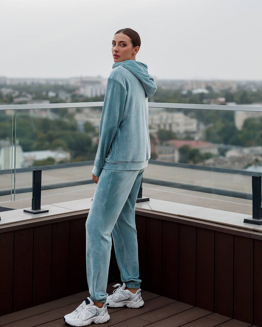 Person wearing a light blue tracksuit standing on a rooftop with a cityscape in the background