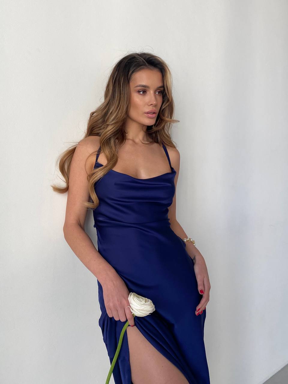 Woman in a blue dress holding a white flower against a plain background