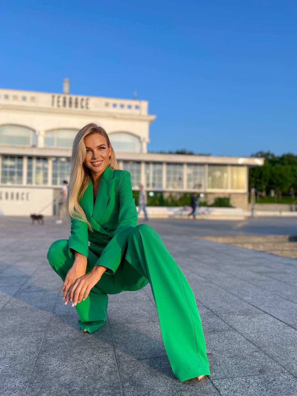 Woman in a green outfit posing outdoors with a building and blue sky in the background