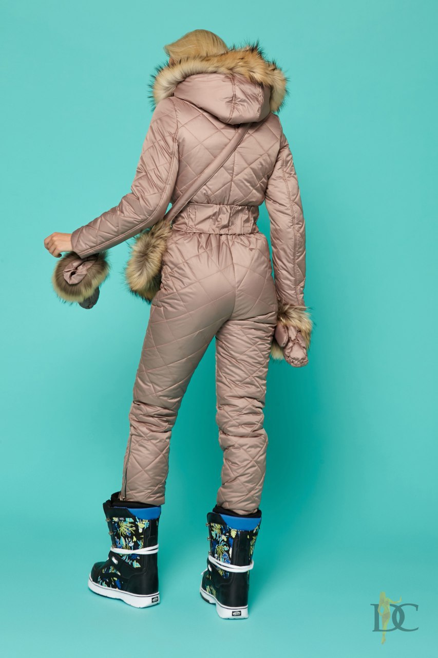 Person wearing a beige winter snowsuit with fur trim on a teal background