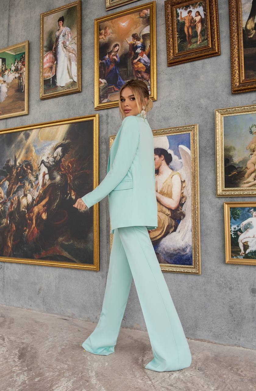 Woman in a light blue suit standing in front of classical art paintings on a wall.