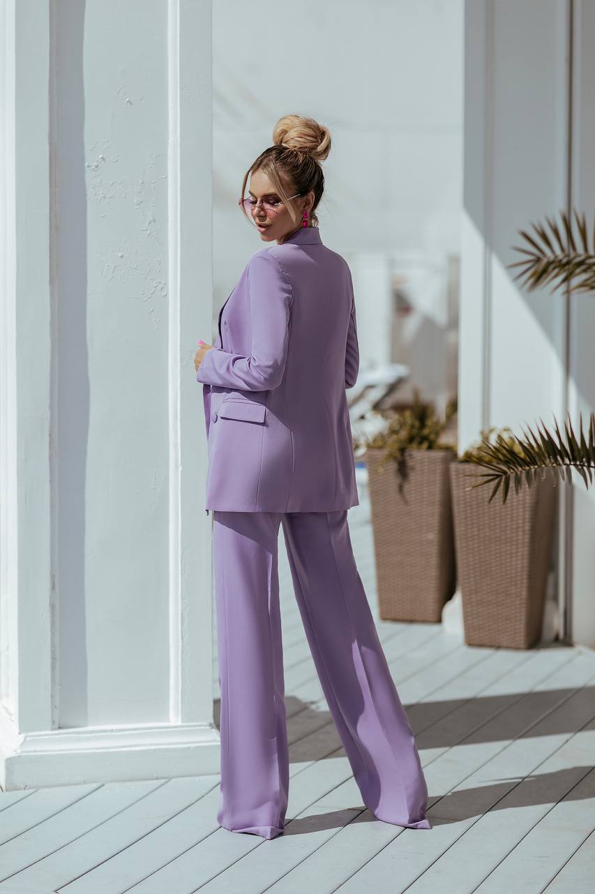 Woman in a lavender suit standing on a wooden deck with plants in the background