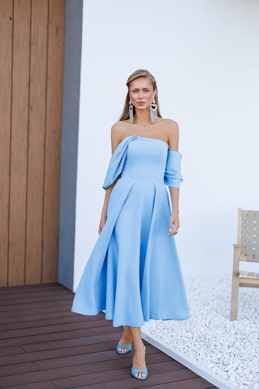 Woman wearing a light blue off-shoulder dress with a matching jacket on a wooden deck.