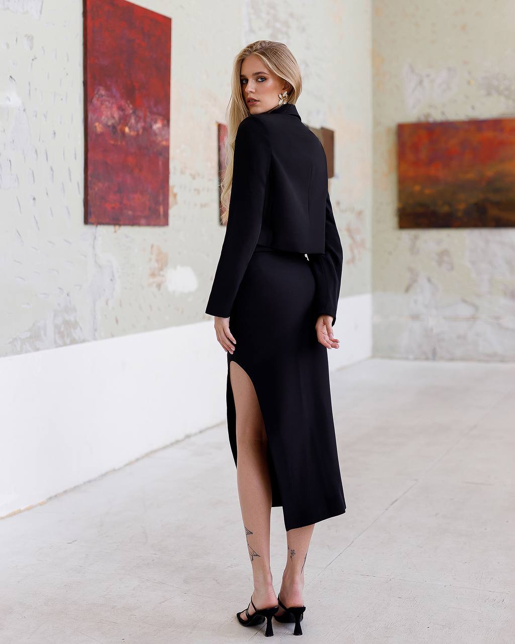 Woman in a black outfit standing in an art gallery with abstract paintings on the wall.