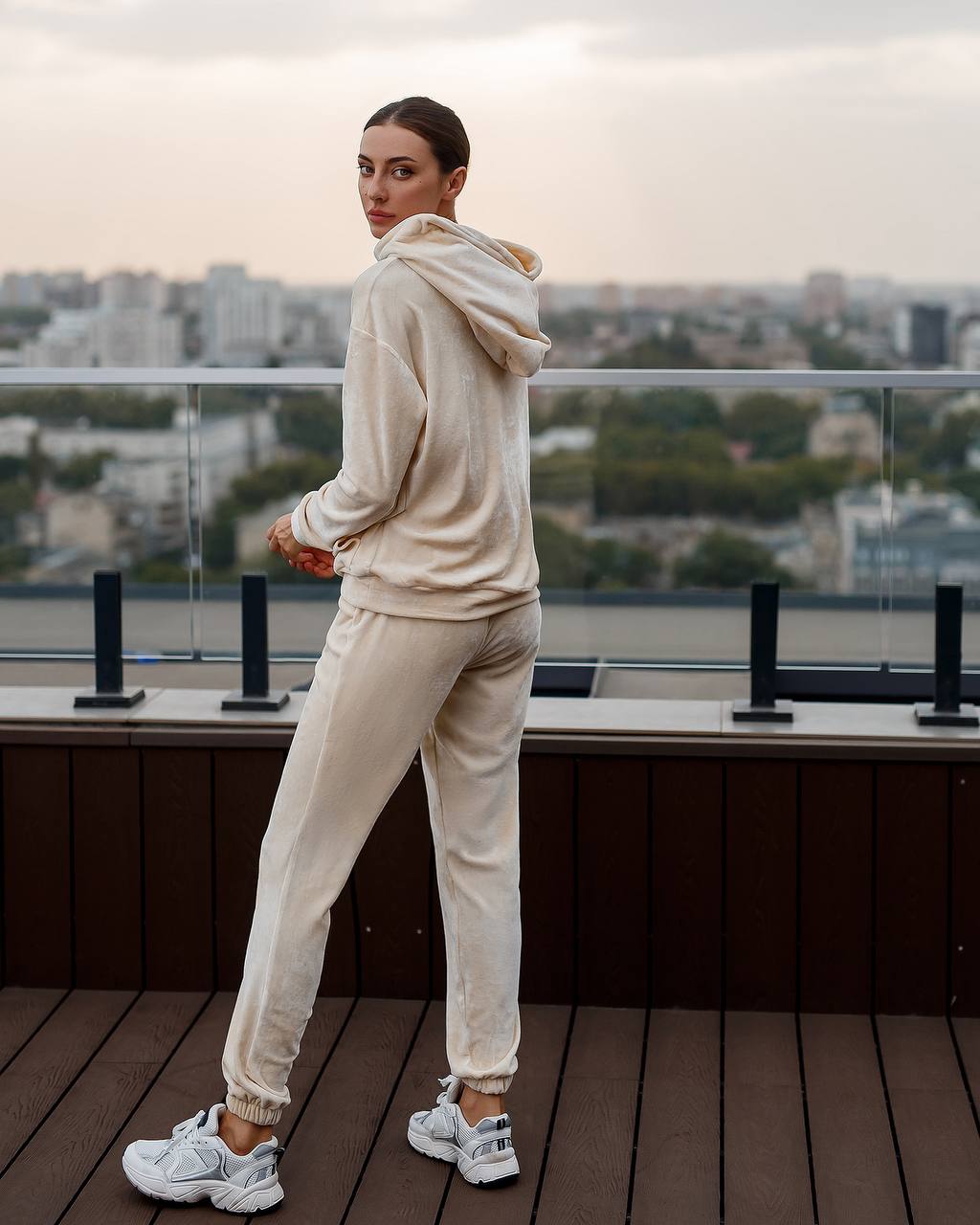 Person wearing a beige hoodie and pants on a rooftop with cityscape view