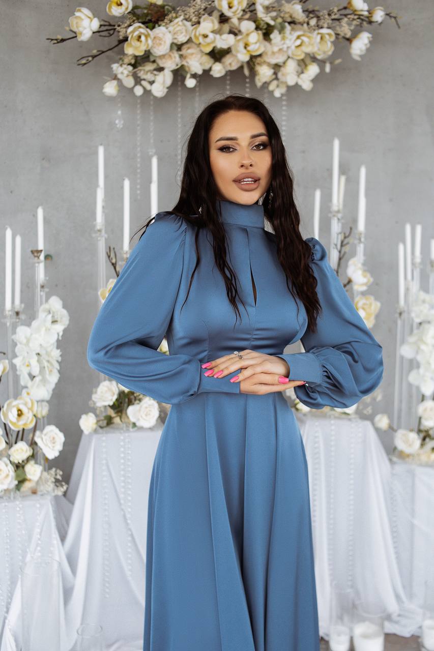 Woman in a blue dress standing in front of a decorative background with flowers and candles.
