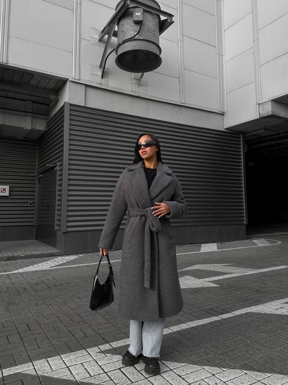 Woman in a gray coat standing on a street with a building in the background