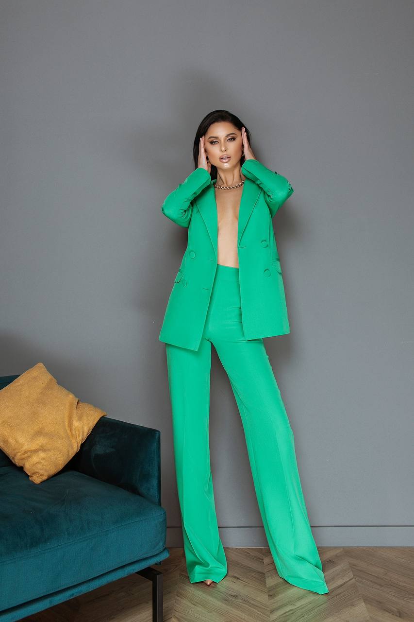 Woman in a green suit standing in a room with a gray wall and teal couch.
