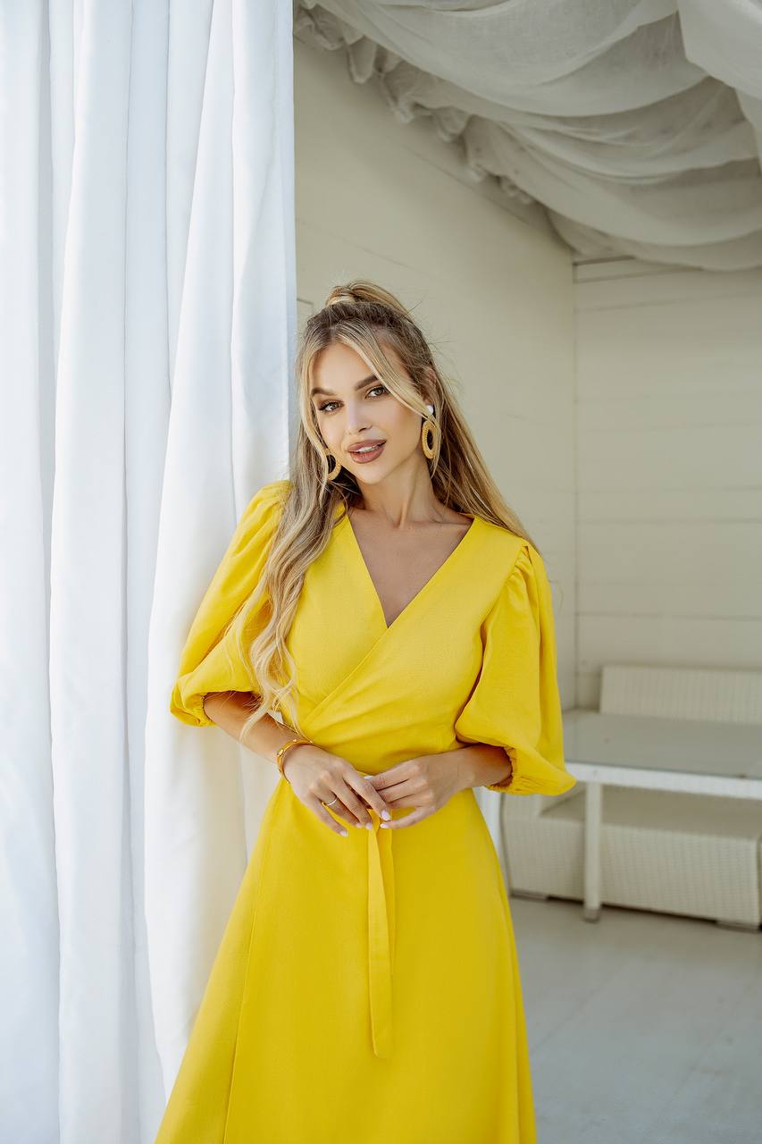 Woman in a yellow dress standing in a bright room with white curtains.