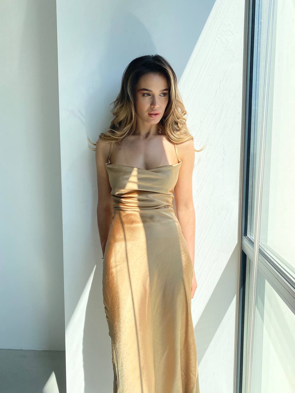 Woman in a gold dress standing against a light-colored wall.