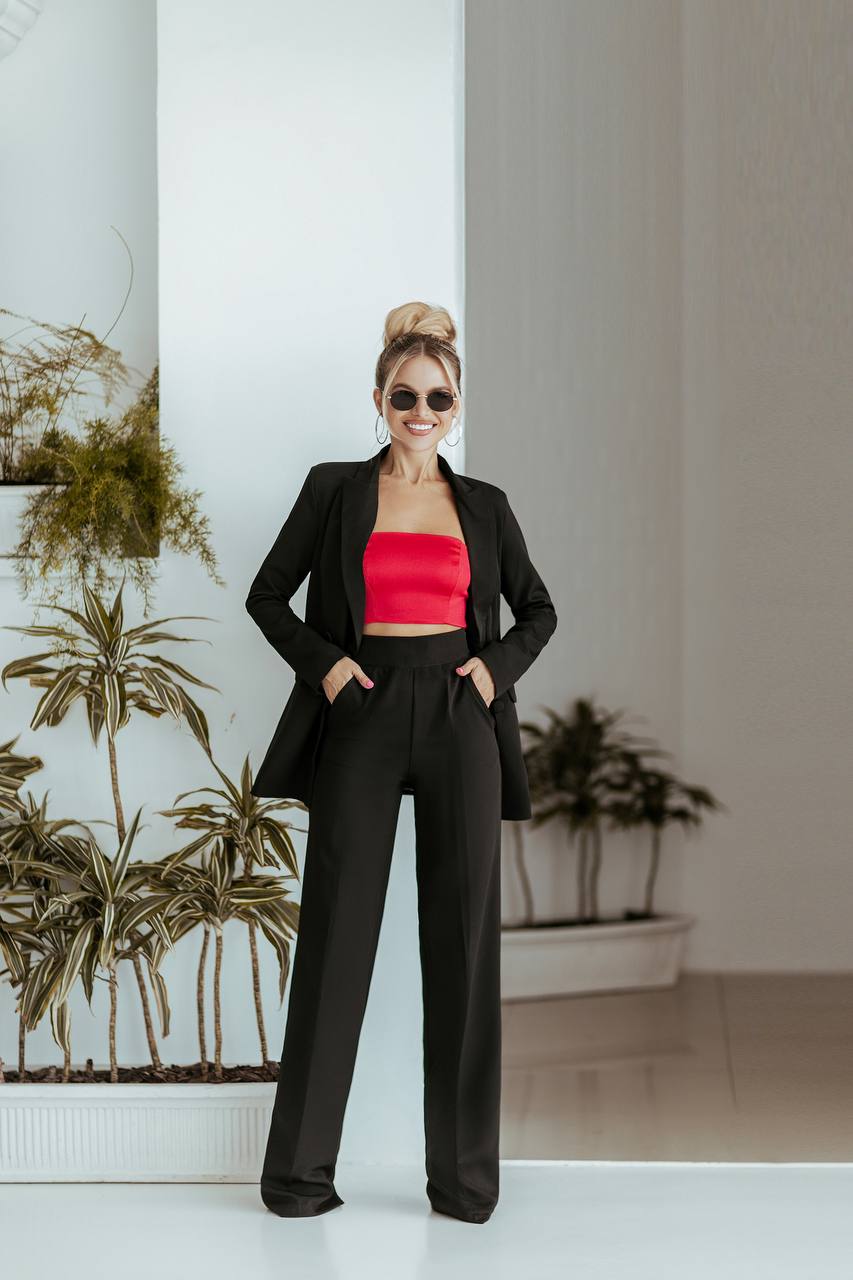 Woman in a black suit with a red top standing in a modern indoor setting.