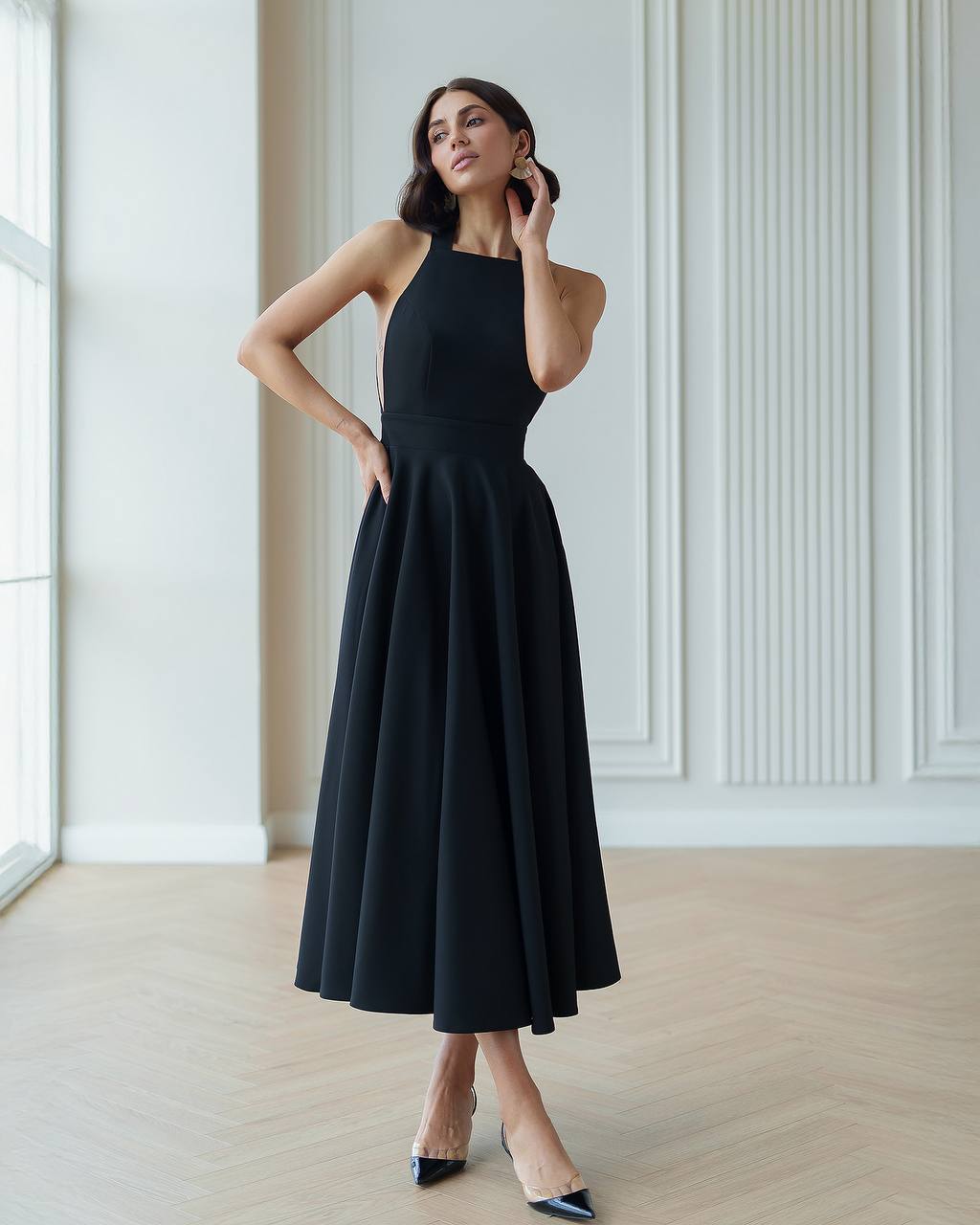 Woman wearing a black dress in a minimalistic room with white walls and wooden floor.