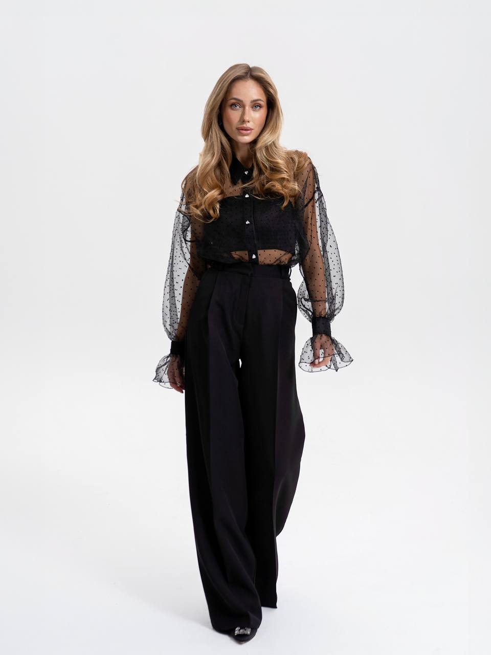 Woman wearing a black outfit with sheer sleeves on a white background