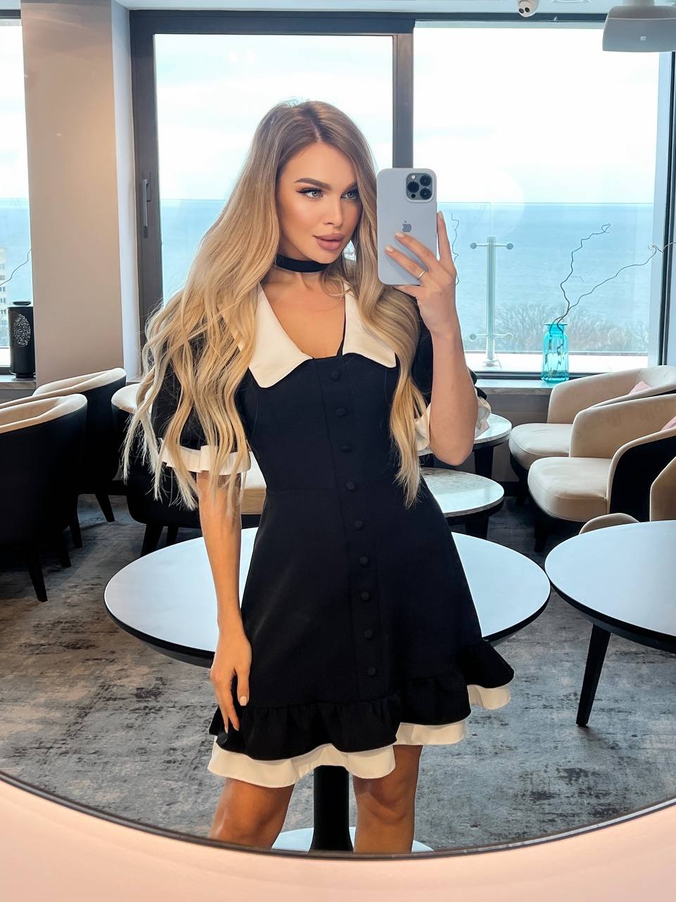 Woman taking a mirror selfie in a stylish black and white dress in a modern interior setting.