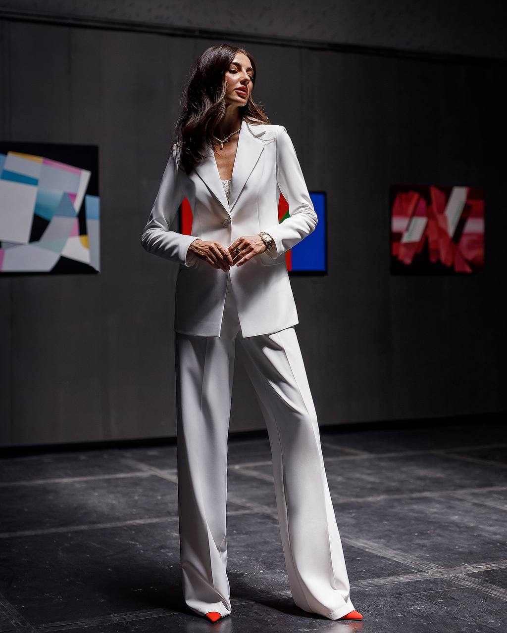 Woman in a white suit standing on a dark floor with colorful abstract art in the background