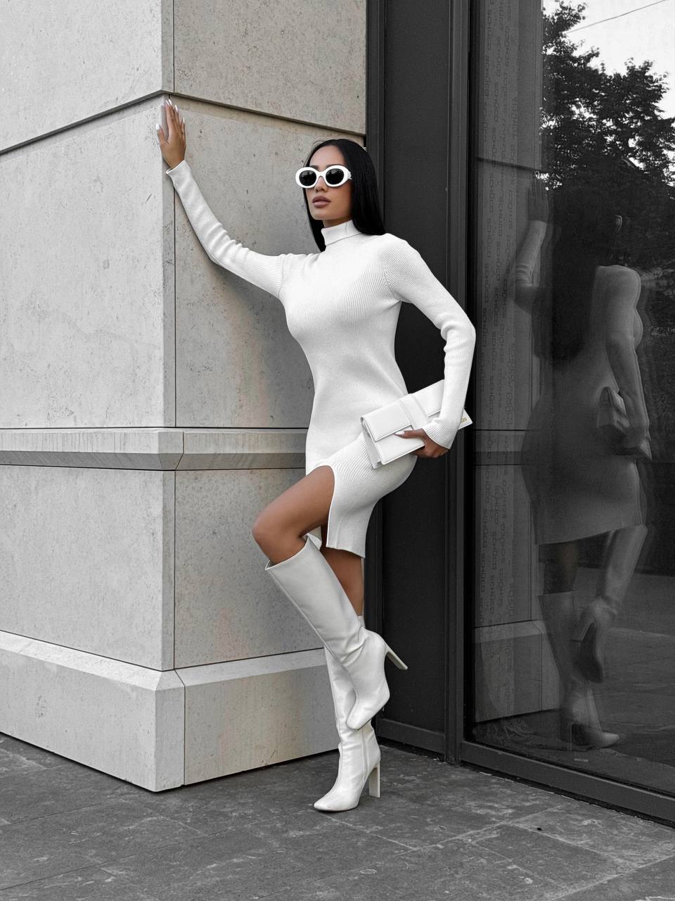 Woman in a white outfit standing against a building with a reflective surface.